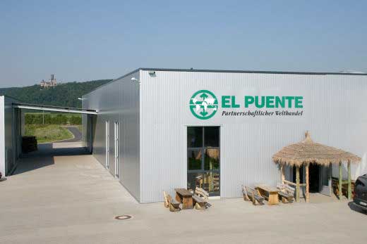 Das moderne Lager von EL PUENTE verleugnet nicht seinen Ursprung. Siehe den Eingang, der exakt einer Kaffeebauern-Hütte nachempfunden ist. Das moderne Lager von EL PUENTE verleugnet nicht seinen Ursprung. Siehe den Eingang, der exakt einer Kaffeebauern-Hütte nachempfunden ist.